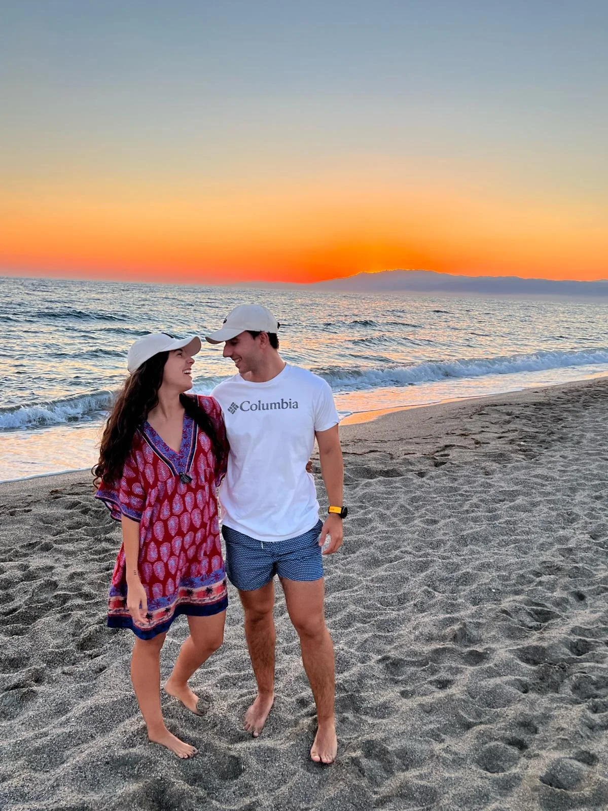 María y Luis caminando por la playa al atardecer